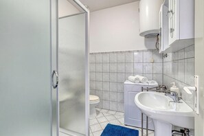 A bathroom with a glass shower door, a toilet, a washing machine, and a sink.