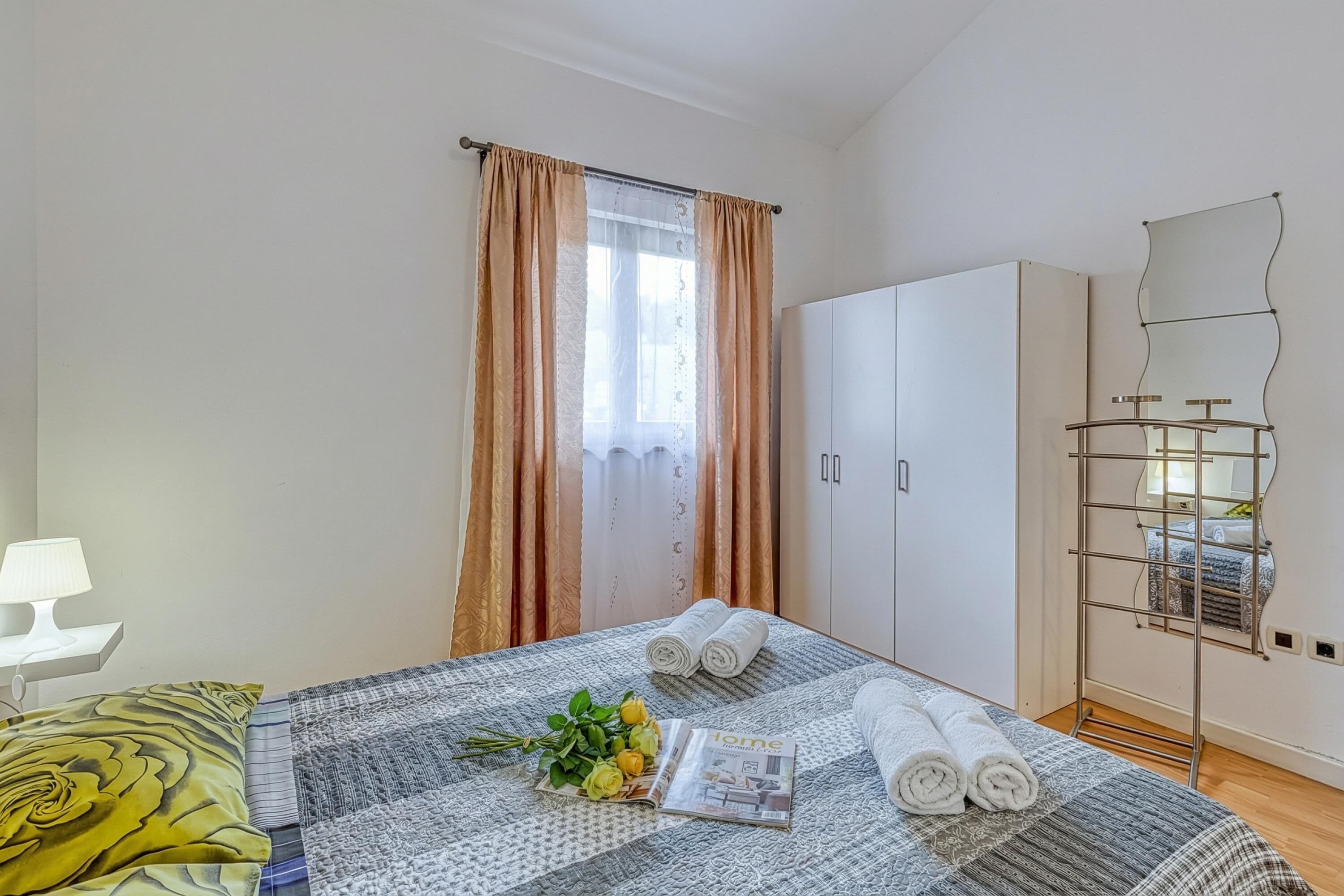 A neatly arranged bedroom with a bed, a bedside table with a lamp, a wardrobe, and a mirror.