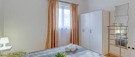 A neatly arranged bedroom with a bed, a bedside table with a lamp, a wardrobe, and a mirror.