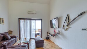 A living room with a sofa, ottoman, and a glass coffee table. There is a TV mounted on the wall and a guitar hanging on the wall. - Pool House Kristina Near Porec (Kastelir-Labinci)