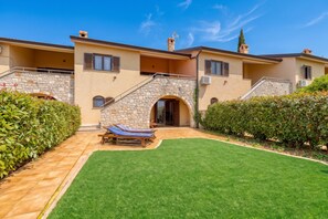 A two-story house with a stone facade, a covered patio, and a well-maintained lawn.