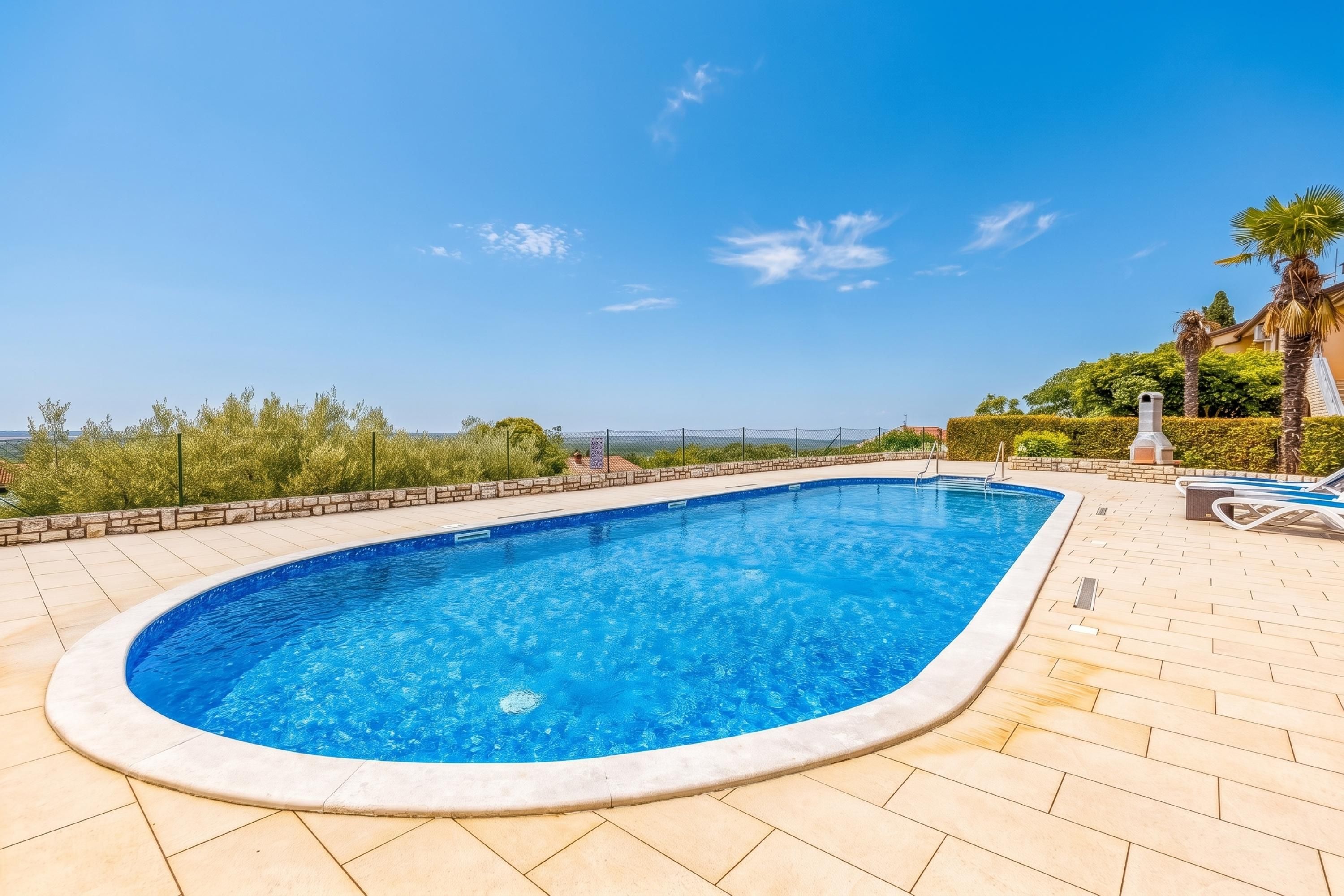 A swimming pool with a clear blue water, surrounded by a tiled deck, and a view of the sky and distant landscape.