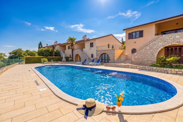 A swimming pool with lounge chairs, a sun hat, and a drink on the edge.