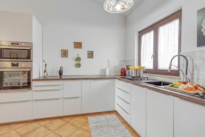 Una cocina moderna con armarios blancos, horno empotrado, pileta y ventana con cortinas.