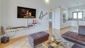 A modern living room with a flat-screen TV, a sofa, a coffee table with a tray of food, and a kitchen in the background. - Pool House Kristina Near Porec (Kastelir-Labinci)