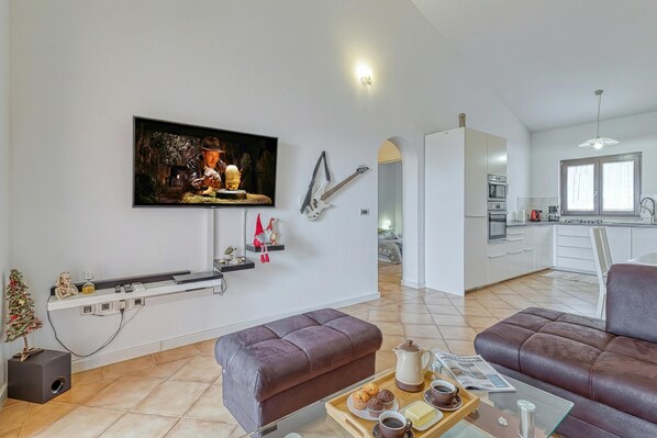 Una sala de estar moderna con un televisor de pantalla plana, un sofá, una mesa de centro con una bandeja de comida y una cocina al fondo.