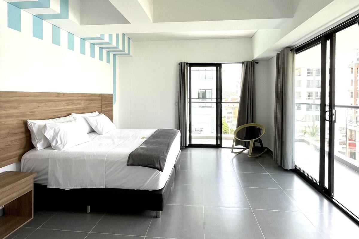 Une chambre d’hôtel moderne dotée d’un grand lit, d’une tête de lit en bois, d’un balcon avec vue et d’un motif géométrique sur le mur.