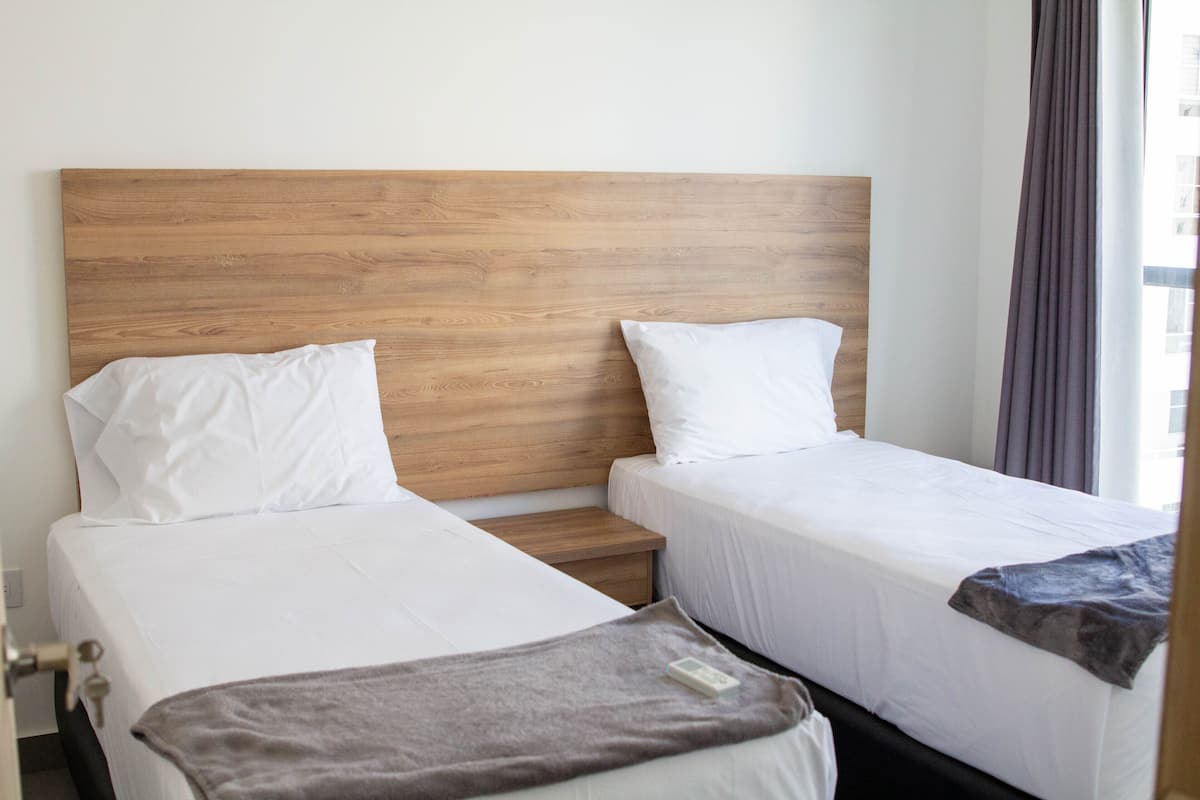 Une chambre d’hôtel avec deux lits, une tête de lit en bois, du linge de lit blanc et une fenêtre avec des rideaux.