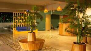 Un vestíbulo con mostrador de recepción, macetas de madera con plantas, suelo con diseño y lámparas colgantes.