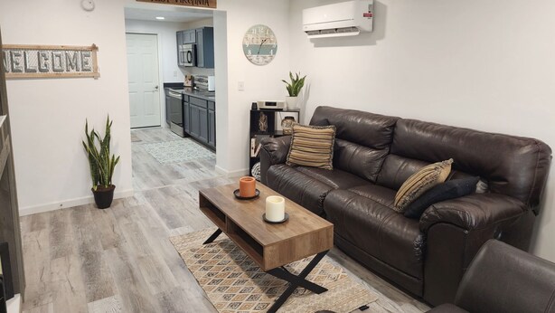 A modern living room with a leather sofa, a wooden coffee table, and a kitchen visible through an open doorway.