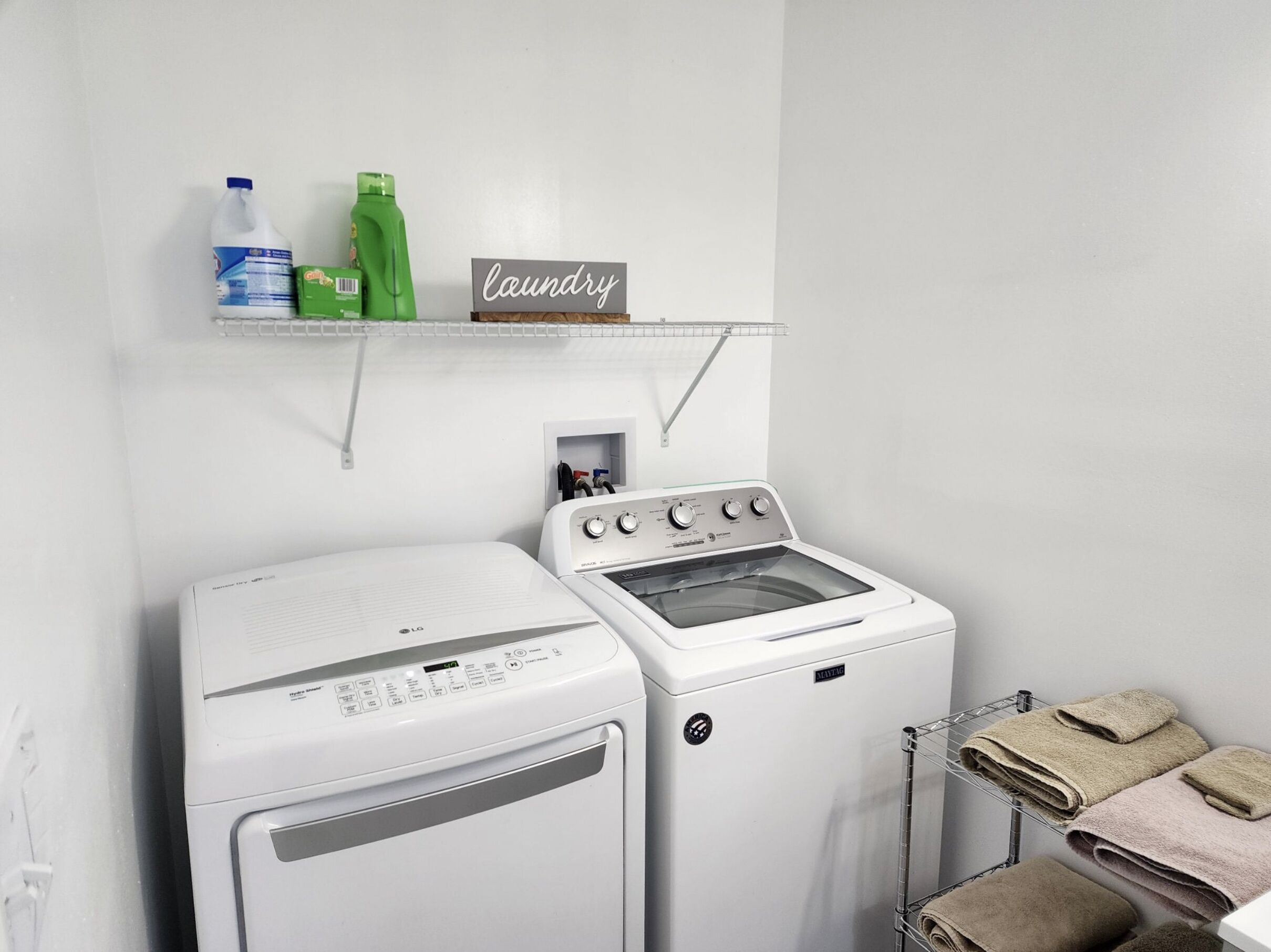 Een wasruimte met een wasmachine, droger en een plank met schoonmaakmiddelen.