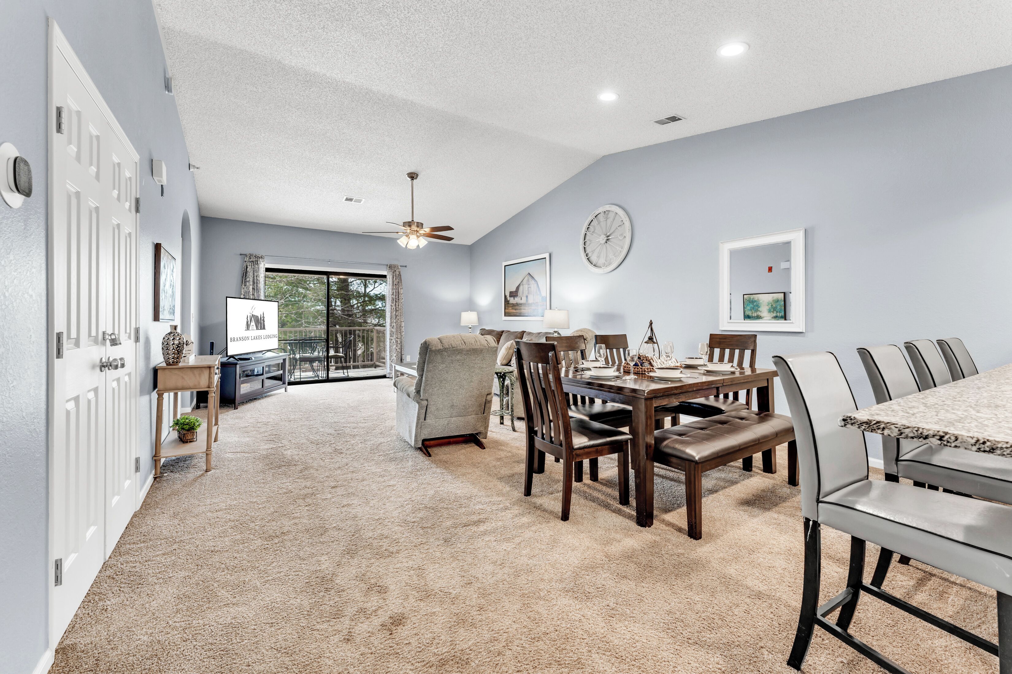 A spacious living room with a large dining table, comfortable seating, and a view to the outside.