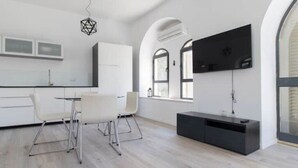Una cocina moderna con armarios blancos, una zona de comedor con mesa y sillas blancas, y un mueble de entretenimiento negro.
