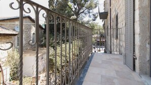 Un estrecho callejón con valla de hierro forjado, edificios de piedra y un árbol.