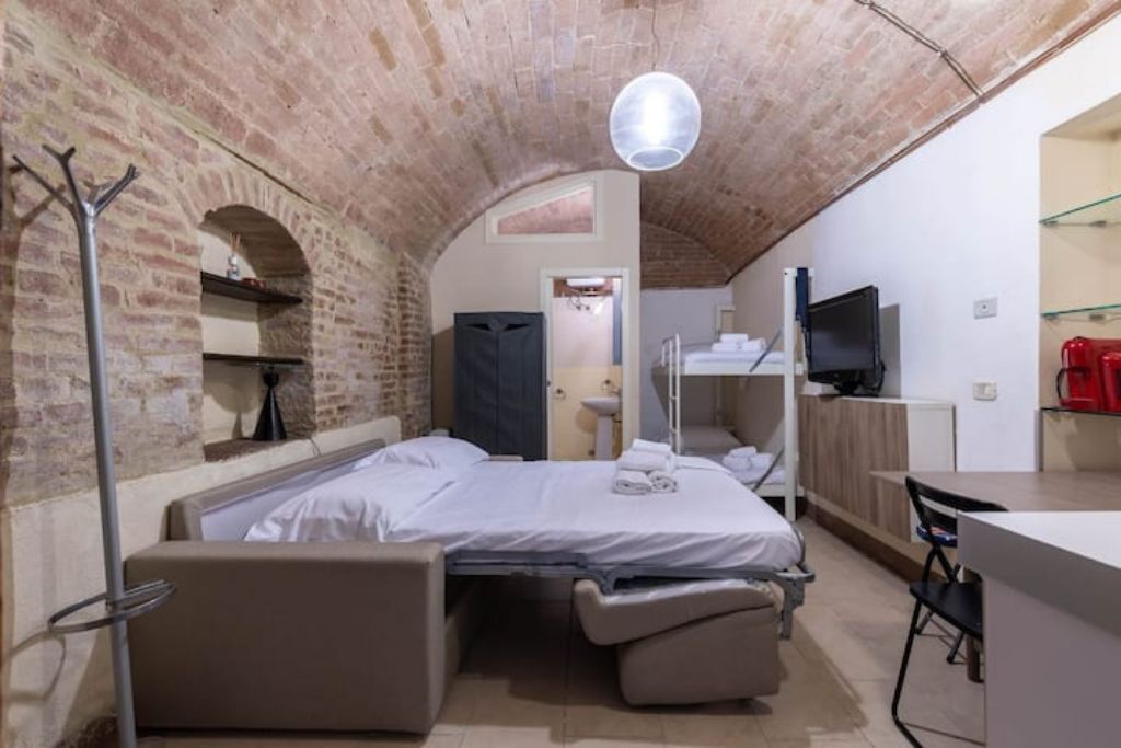 Una habitación pequeña con cama, escritorio y televisión.