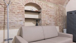 Una stanza con parete in mattoni, un divano, un appendiabiti e un termosifone.
