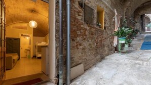 Un corridoio interno con parete in mattoni, una porta che dà su un bagno e una scala.