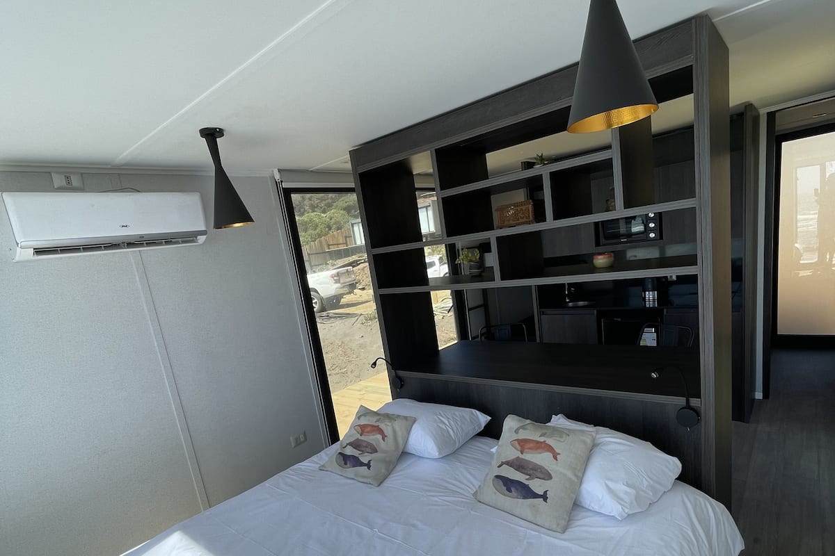 A bedroom with a bed, pillows, a shelf unit, and an air conditioning unit.