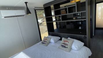 A bedroom with a bed, pillows, a shelf unit, and an air conditioning unit.