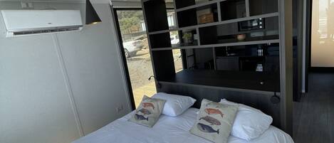 A bedroom with a bed, pillows, a shelf unit, and an air conditioning unit.