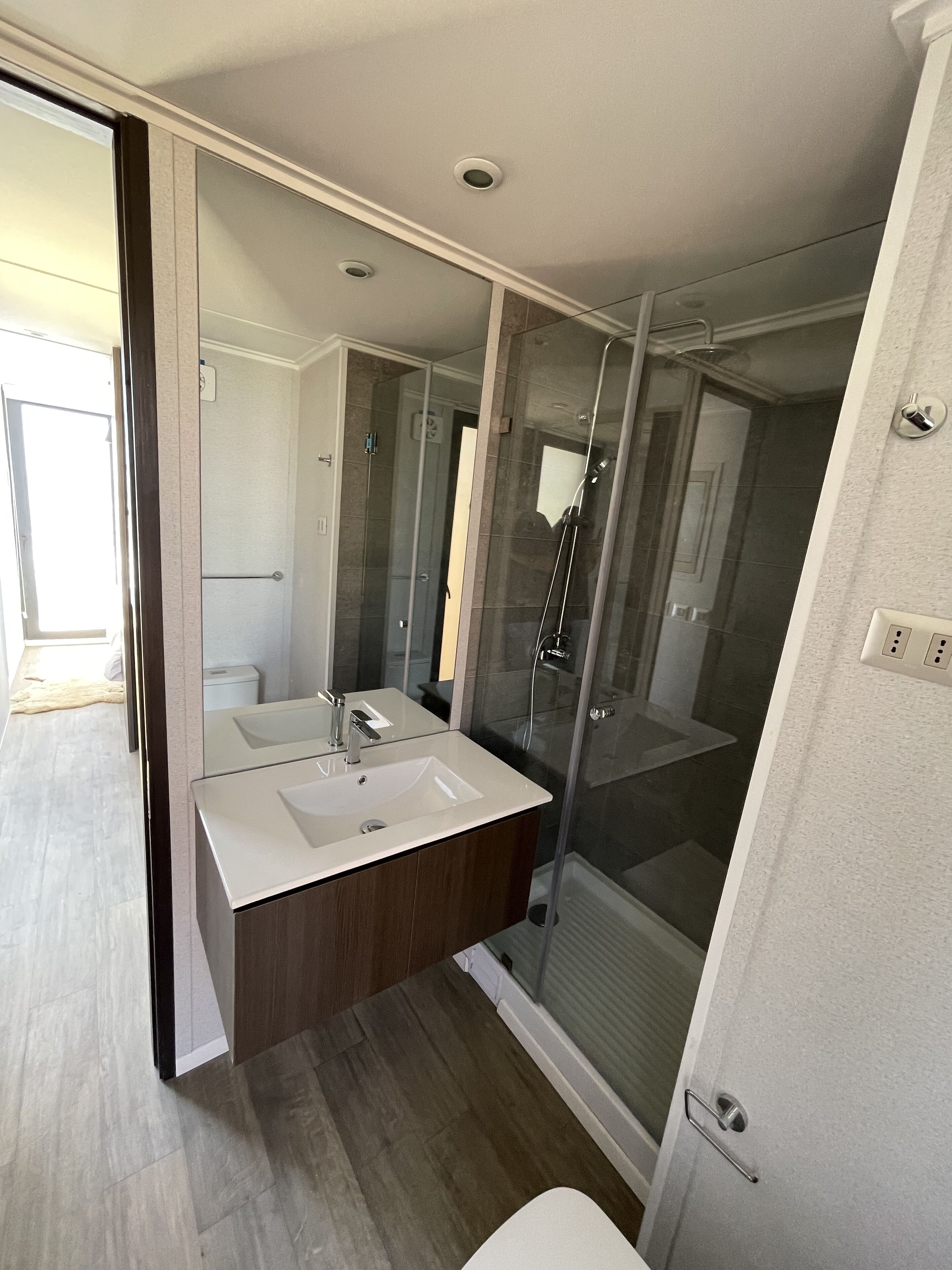 A modern bathroom with a glass-enclosed shower, a double vanity with a mirror, and a light-colored floor.