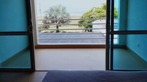 Ein Zimmer mit einer Schiebeglastür, die auf einen Balkon mit Blick auf den Strand und Palmen führt.