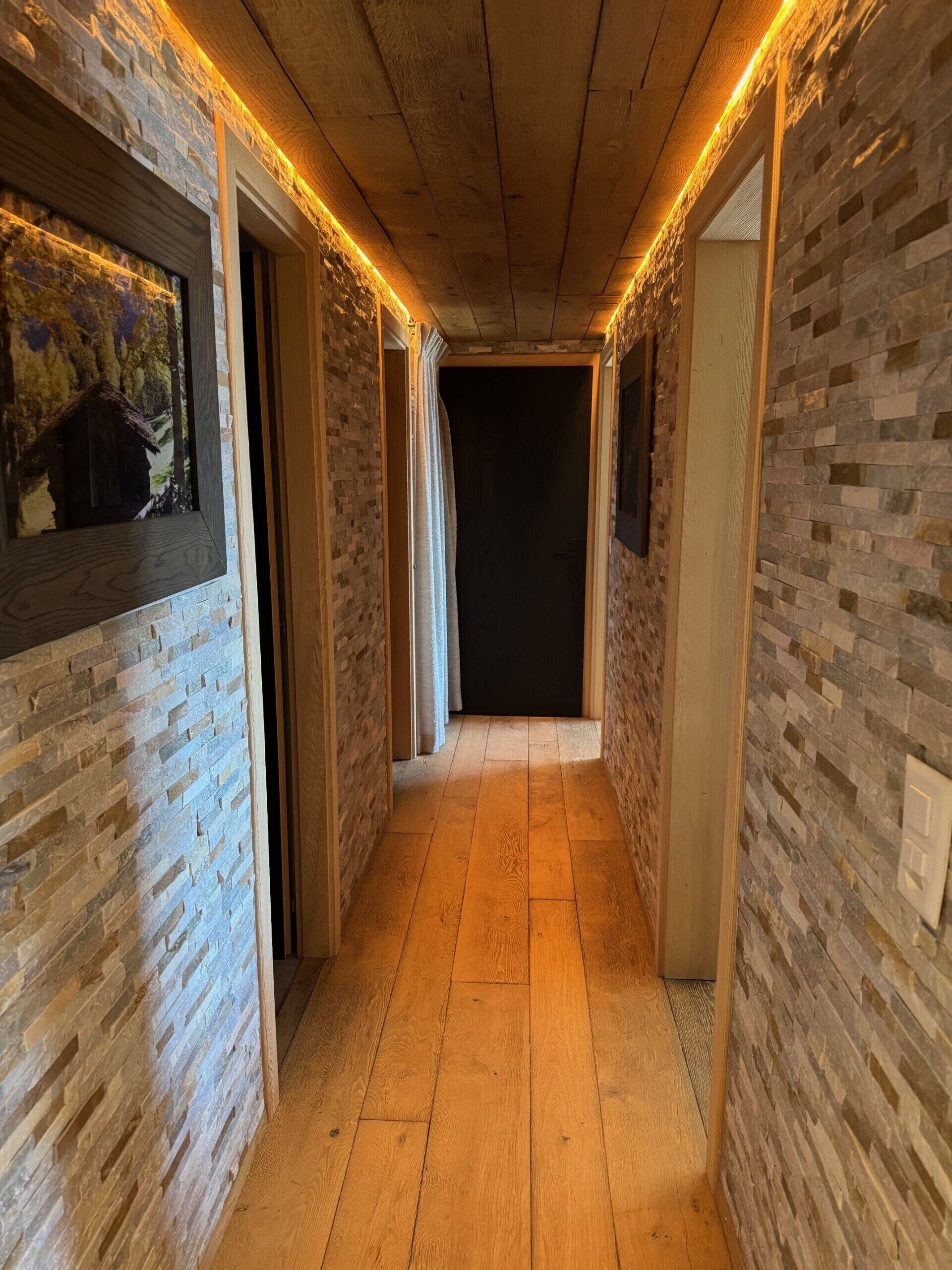 A hallway with brick walls and wooden flooring, leading to a dark room.