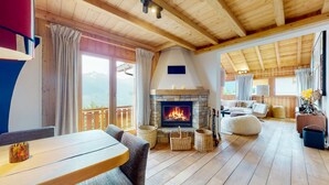 A cozy living room with a stone fireplace, wooden floors, and a balcony with curtains. - Arnold LUXE & COSY Chalet for 14 People in Les Masses (Les Masses)