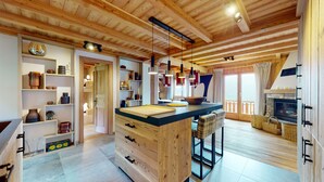A modern kitchen with wooden beams, a central island, pendant lighting, and a fireplace. - Arnold LUXE & COSY Chalet for 14 People in Les Masses (Les Masses)