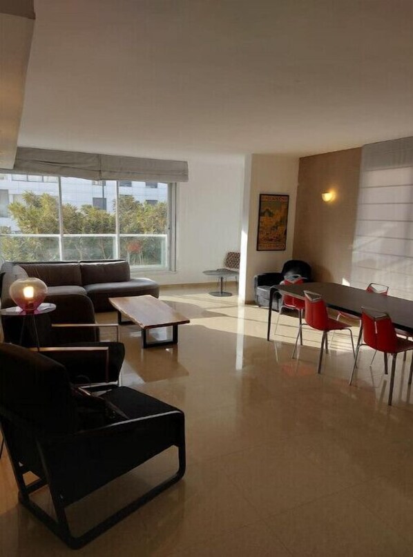 Relax in this stylish living room with a large window offering a view of the outdoors, a comfortable sofa, and a dining area.