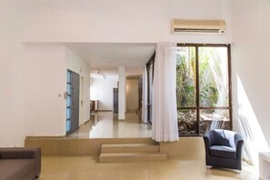A spacious living area with a staircase leading to another room, a large window with curtains, and a modern air conditioning unit.