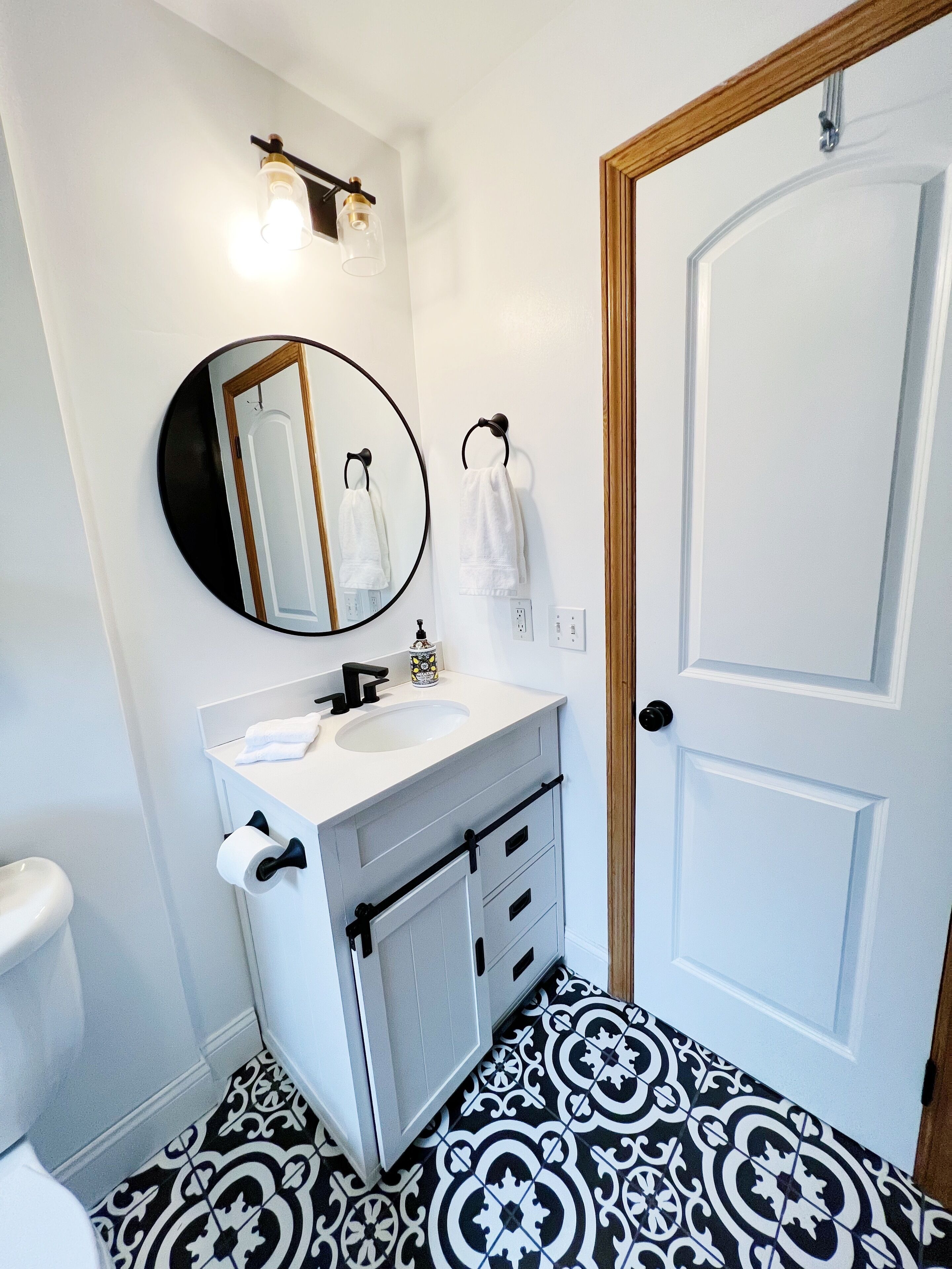 Un baño con un lavabo blanco, un espejo, un perchero para toallas y un suelo con diseño.
