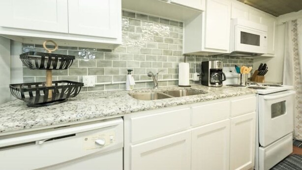 A kitchen with white cabinets, a granite countertop, a stainless steel sink, a microwave, and a stove. - Downtown Hideaway on trendy Denton square (Denton)