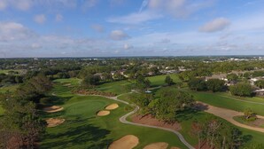 Een golfbaan met zandbunkers, bomen en een heldere lucht.