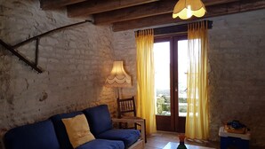 Un soggiorno accogliente con un divano blu, un tavolino in legno, una lampada e una vista attraverso una finestra con tende gialle.