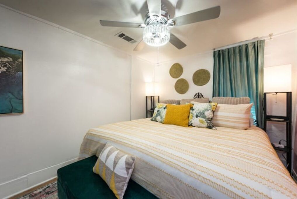 A bedroom with a bed, a ceiling fan, a chandelier, a green bench, and a wall with circular decorations.