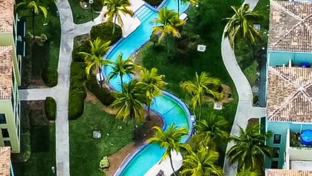 An aerial view of a resort with winding pools, palm trees, and a mix of modern and traditional architecture. - Aquatika Happy Place *pools and beach access* (Medianía Alta)