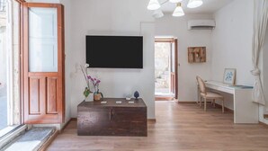 A modern living room with a wooden bench, a mounted TV, a desk with a chair, and a large window with a view. - Dione terrace double flat by Dimore in Sicily (Syracuse)