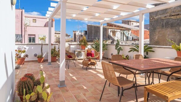 An outdoor patio with a table and chairs, surrounded by potted plants and a pergola structure. - Dione terrace double flat by Dimore in Sicily (Syracuse)
