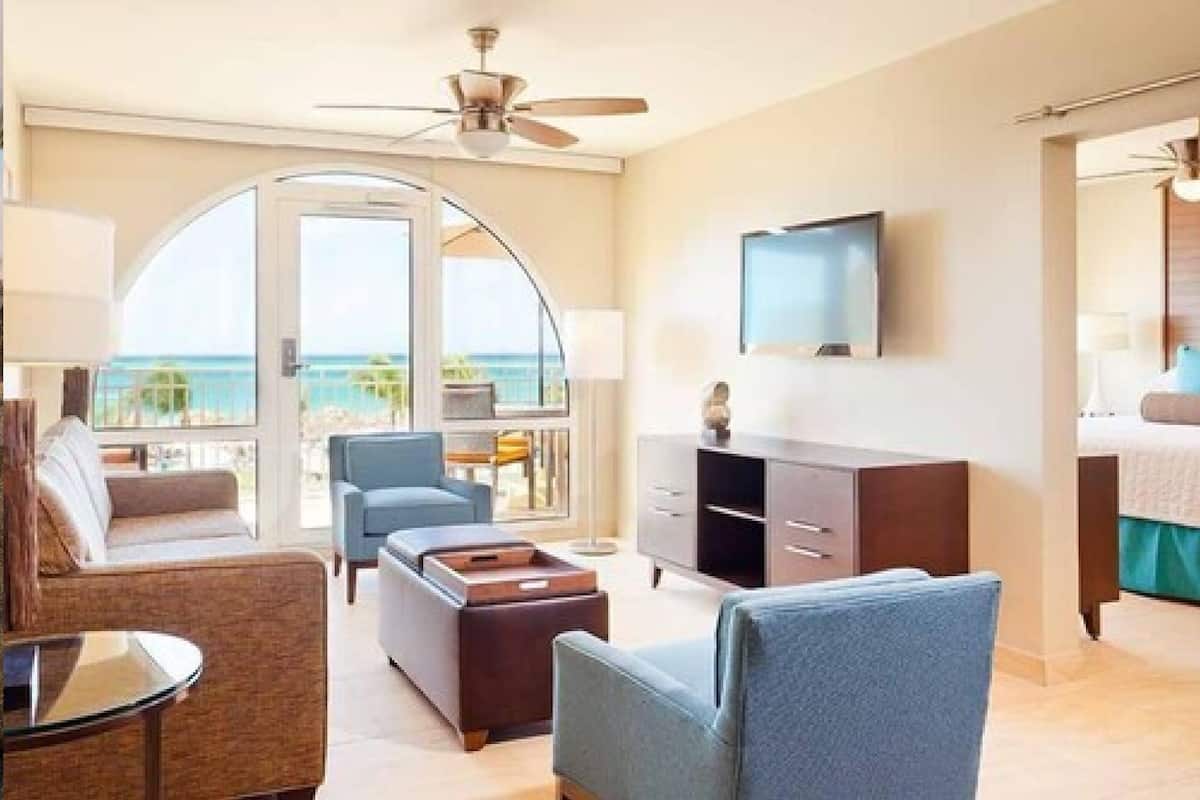 Una habitación de hotel con balcón, televisión, sofá, mesa de centro y escritorio.
