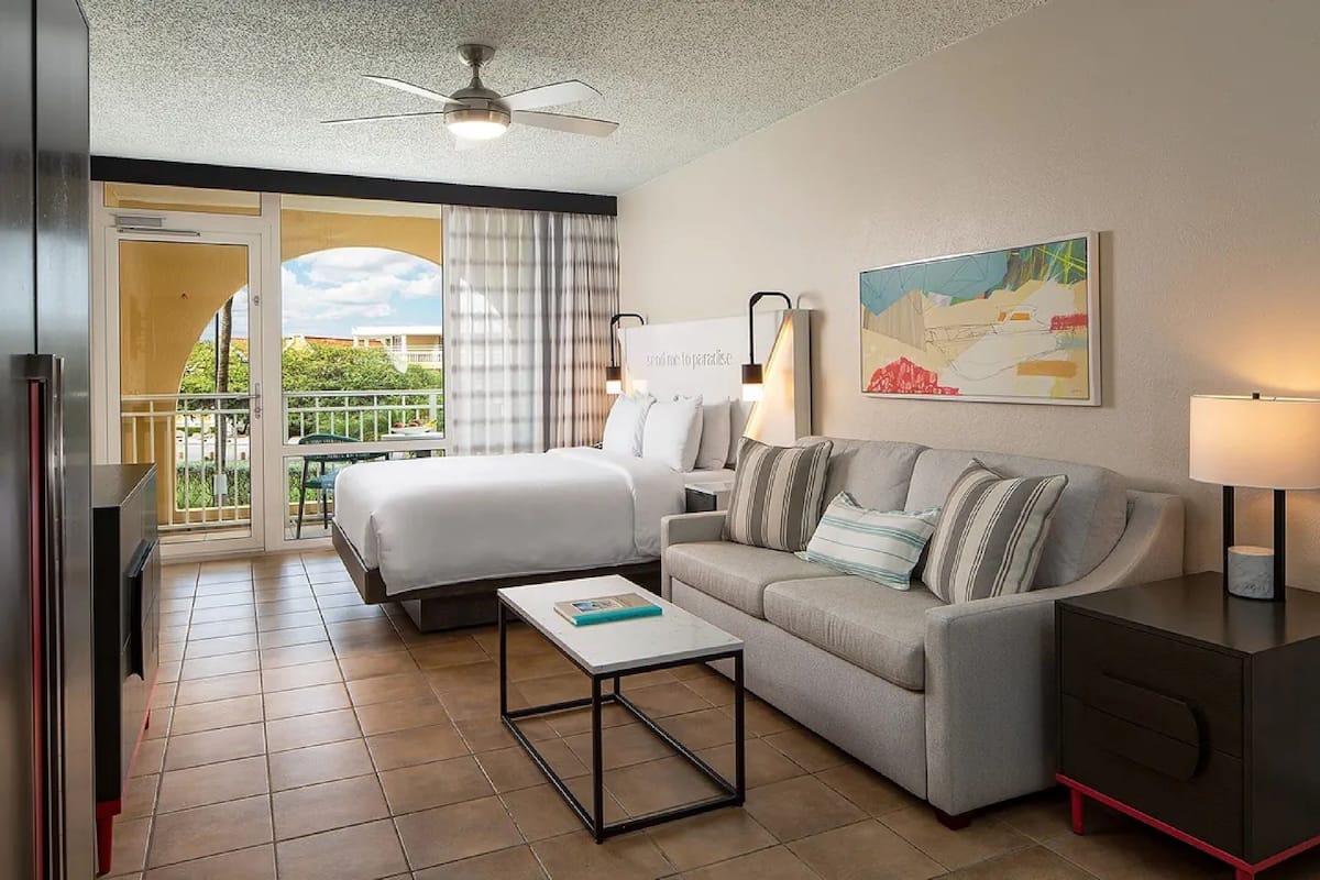 Una habitación de hotel con cama, sofá, mesa de centro, escritorio y balcón con vistas.