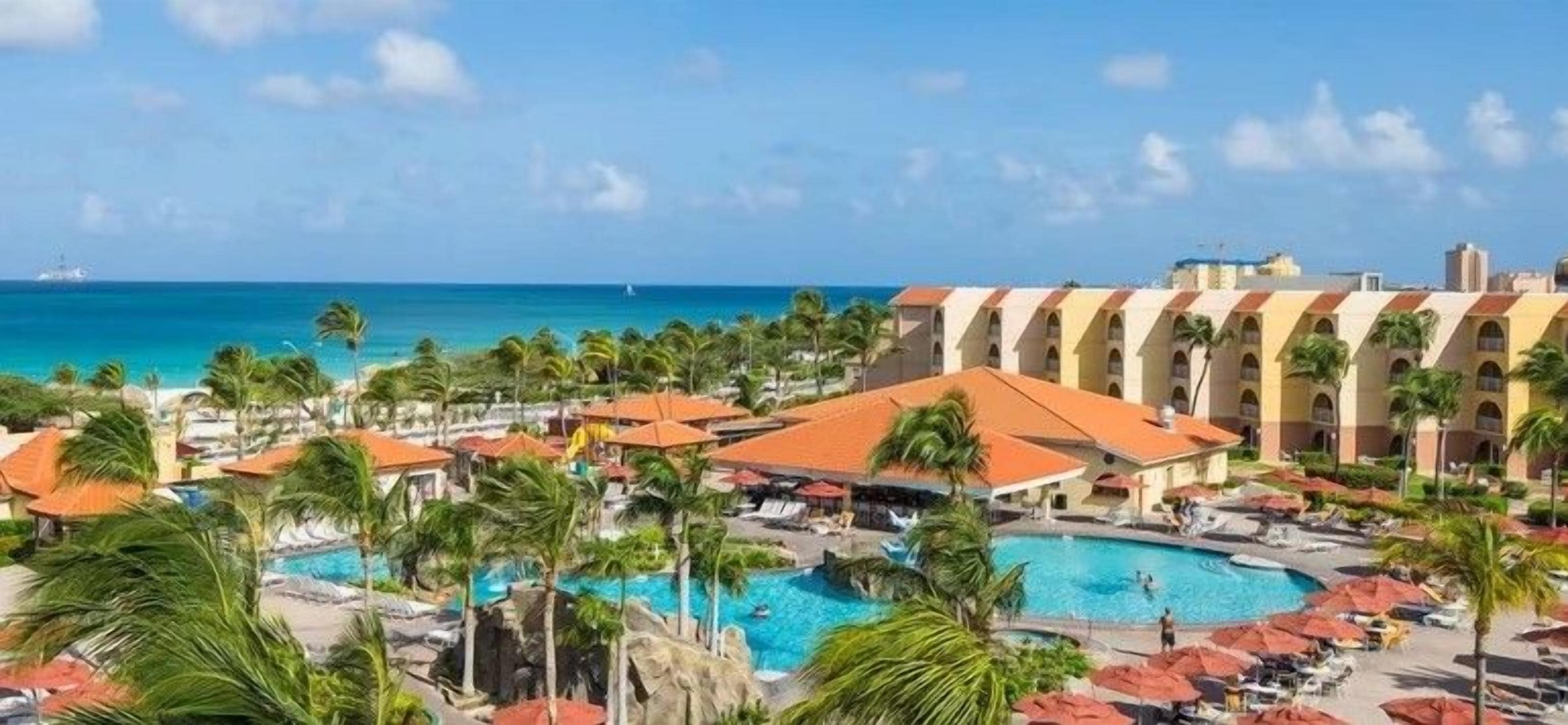 A resort with a large pool, palm trees, and a view of the ocean.