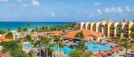 A resort with a large pool, palm trees, and a view of the ocean.
