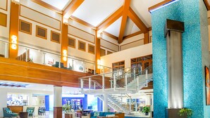 Un hall d’entrée spacieux avec un plafond haut, des poutres en bois, un escalier et un espace détente comprenant des chaises et des tables.