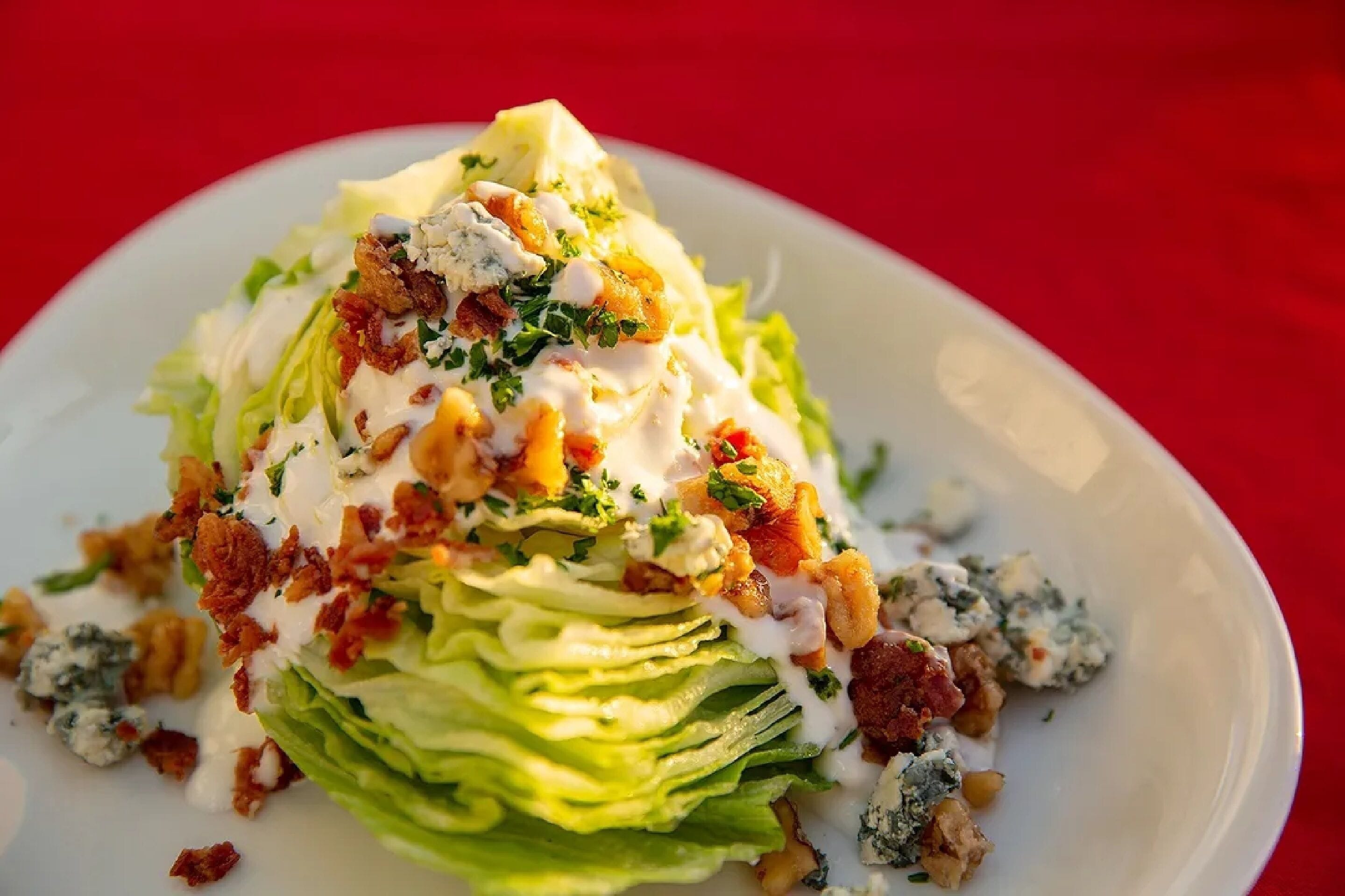 A salad with lettuce, blue cheese, bacon, and a creamy dressing on a white plate.