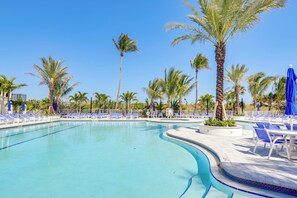 A swimming pool with blue lounge chairs and palm trees. - Sunny Ocean Village Beach Condo: Community Pool (Fort Pierce)