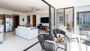 A modern living room with a white sofa, black chairs, a dining area, and a balcony with a glass railing. - Modern 2BR Golden Zone | Top Floor | Ocean View (Bucerias)