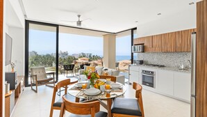 A modern kitchen with a large island, a dining area with a view, and a balcony with a cityscape view. - Modern 2BR Golden Zone | Top Floor | Ocean View (Bucerias)