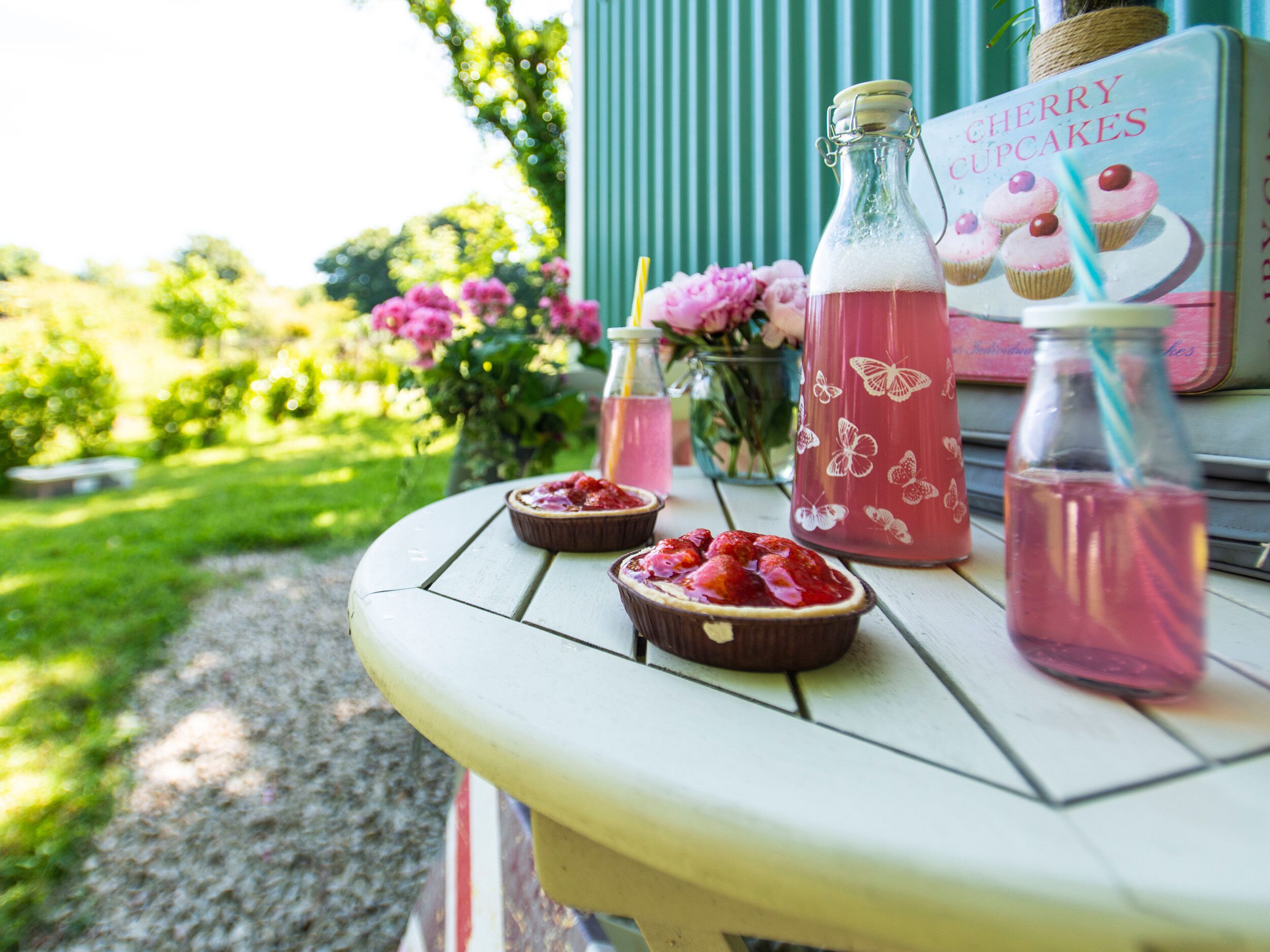Une table avec une bouteille de mini-muffins aux cerises, un verre d’une boisson rose et deux petits bols de nourriture.