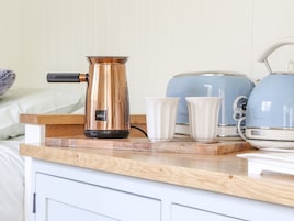 Una encimera de cocina con una cafetera, dos tazas blancas y un electrodoméstico azul.